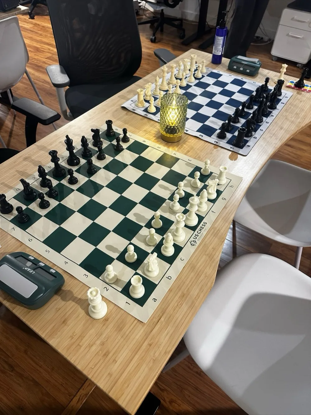 Two chess boards with digital clocks mid-game on a wooden table